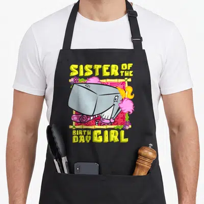 Pearl birthday apron - Cartoon cake slice in bamboo frame with Sister of the Birthday Girl text — shown on a black cotton canvas apron against a white background
