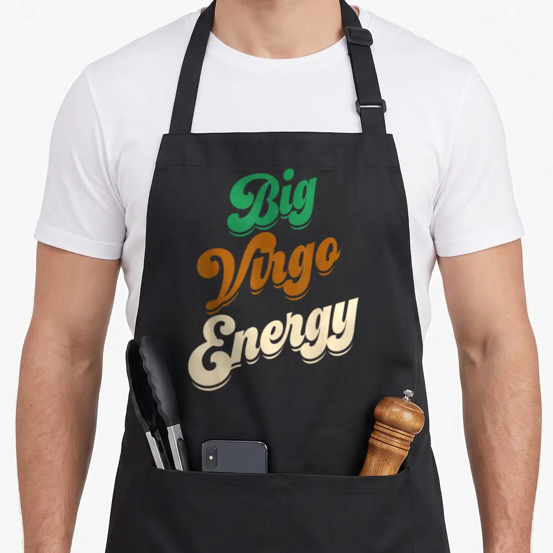 Energy zodiac aprons - Stacked Big Virgo Energy text in green orange and cream retro script — shown on a black cotton canvas apron against a white background