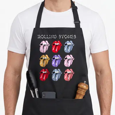 Multi tongue rolling stones apron - Nine mouths with tongues in red blue orange purple pink grid below text — shown on a black cotton canvas apron against a white background