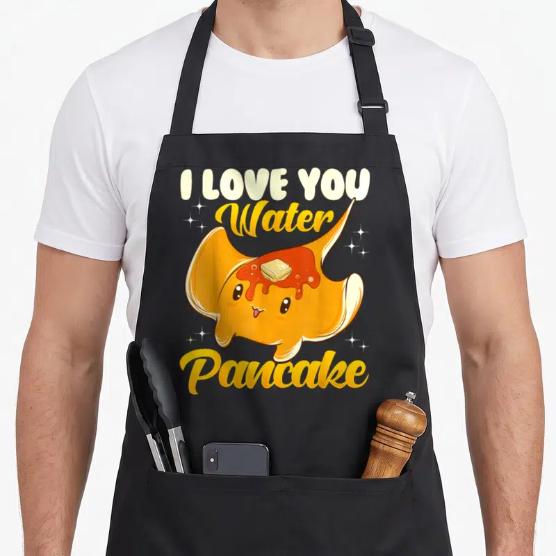 Water pancake apron - Cartoon orange stingray with butter syrup and text I LOVE YOU Water Pancake — shown on a black cotton canvas apron against a white background