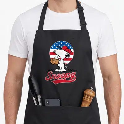 Americana baseball apron - Cartoon dog with brown glove in front of circular red white blue flag and red Snoopy text — shown on a black cotton canvas apron against a white background