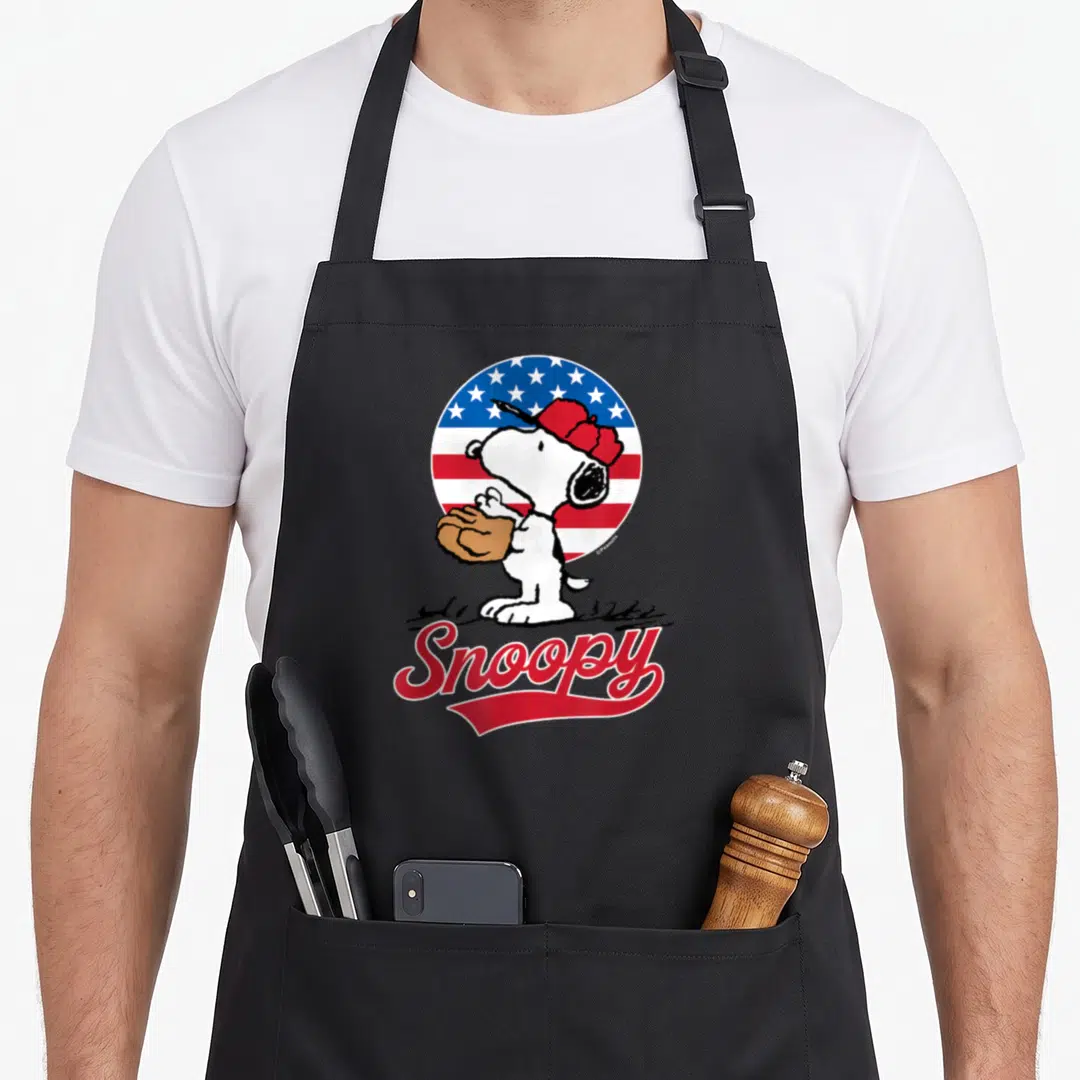 Americana baseball apron - Cartoon dog with brown glove in front of circular red white blue flag and red Snoopy text — shown on a black cotton canvas apron against a white background
