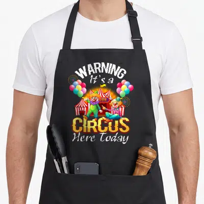 Carnival birthday apron - Two clowns and circus tent with WARNING It's a CIRCUS Here Today text — shown on a black cotton canvas apron against a white background