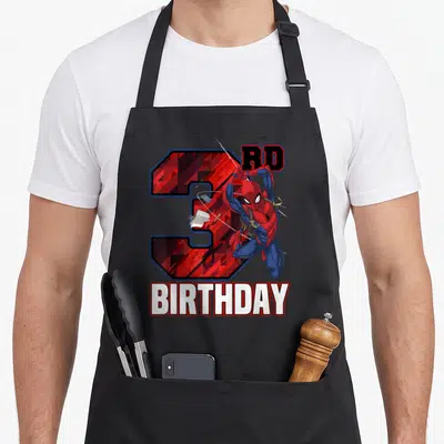 Swing birthday apron - Spider-Man leaping over red number 3 with RD and BIRTHDAY text in cartoon style — shown on a black cotton canvas apron against a white background