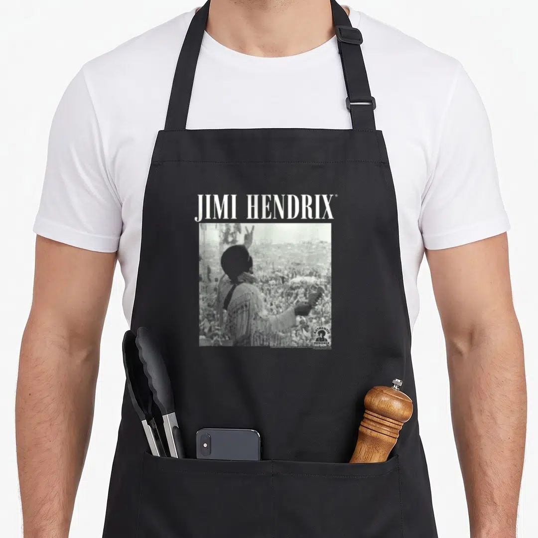 Jimi woodstock era apron - JIMI HENDRIX text above square B&W photo of musician with raised hand facing crowd — shown on a black cotton canvas apron against a white background