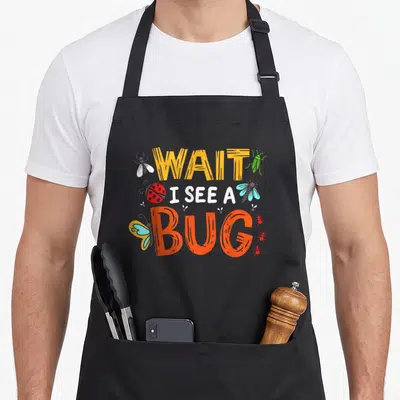 Bug crazy insect lover apron - Cartoon bugs and stacked text reading WAIT I SEE A BUG in yellow, orange, red, blue — shown on a black cotton canvas apron against a white background