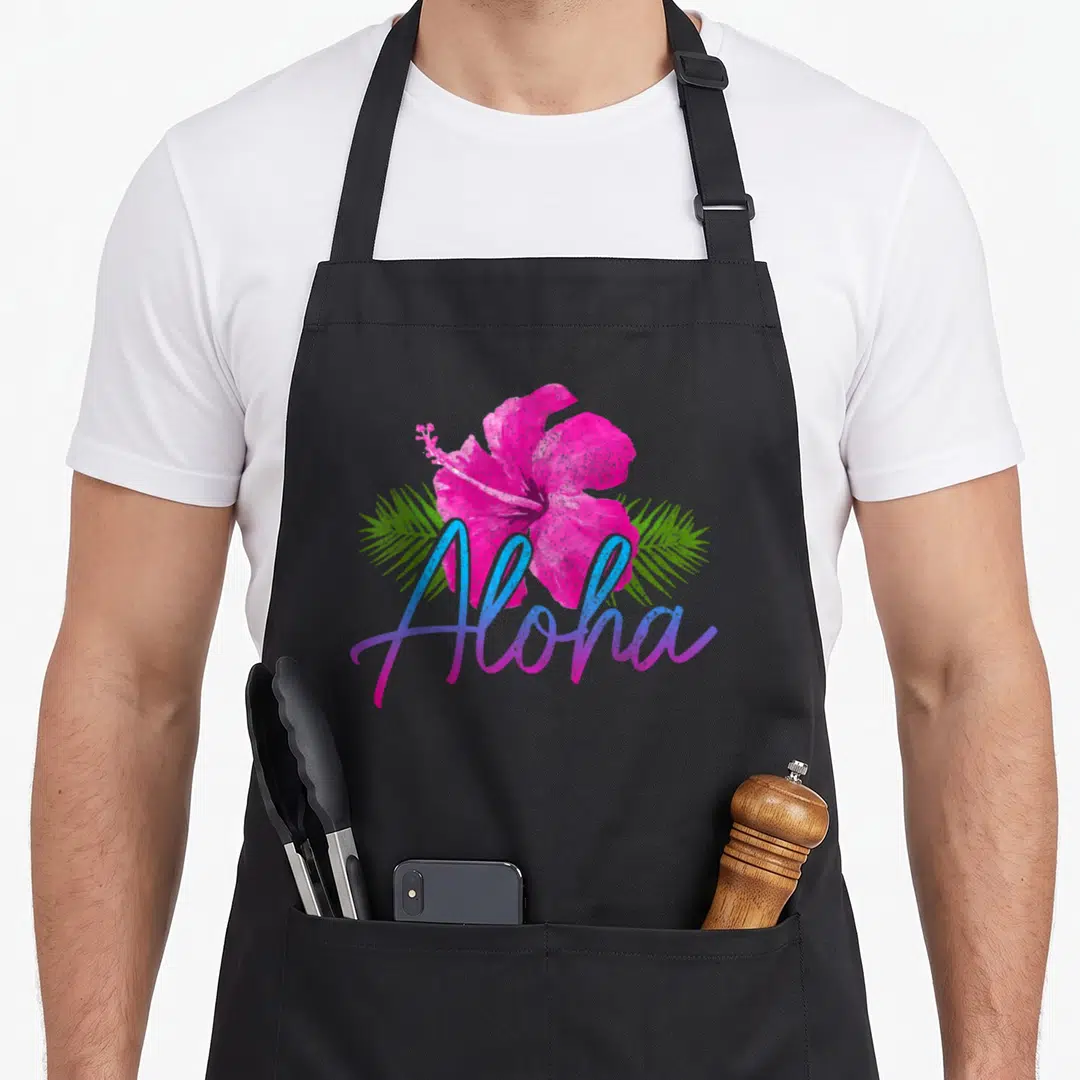 Hibiscus hawaiian apron - Pink hibiscus with green palm leaves and gradient Aloha script in watercolor style — shown on a black cotton canvas apron against a white background