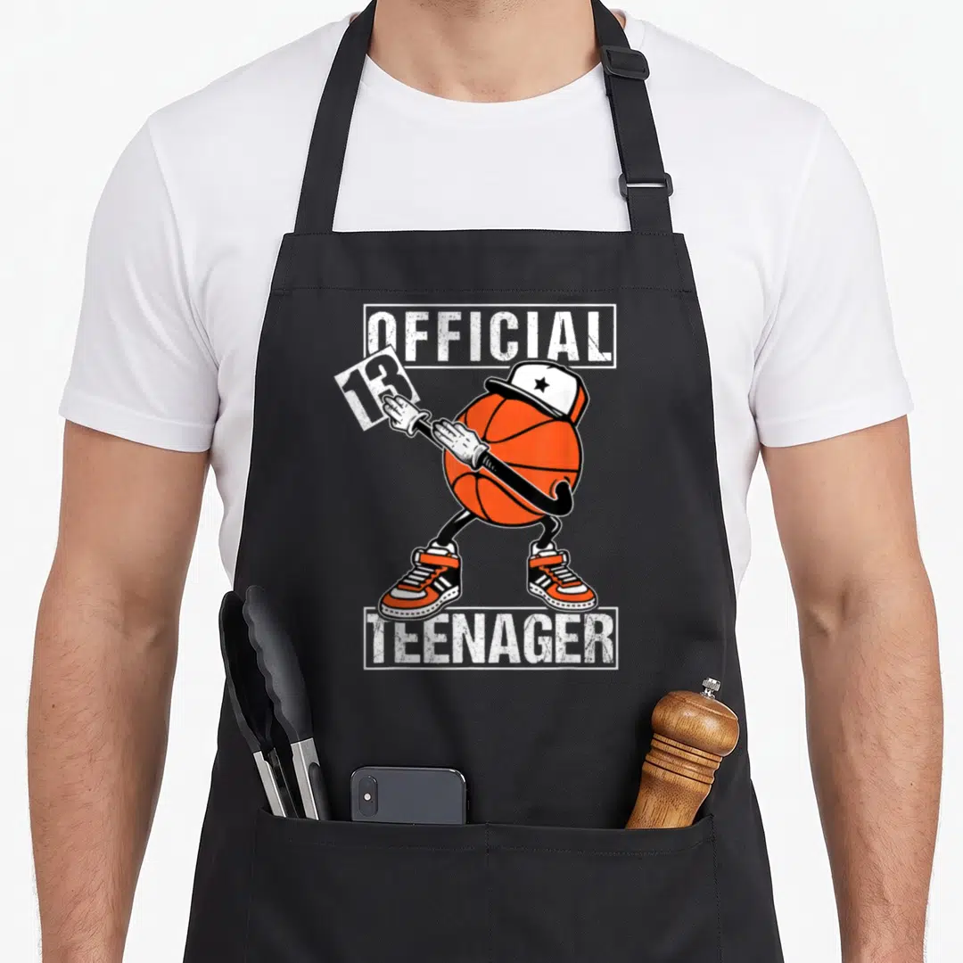 13th basketball birthday apron - Dabbing orange basketball character wearing cap and sneakers with OFFICIAL 13 TEENAGER — shown on a black cotton canvas apron against a white background