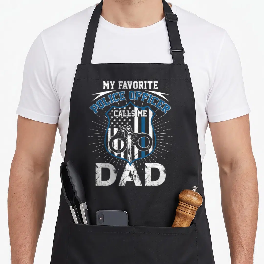 Police officer father day apron - Distressed blue and white badge with handcuffs and flag stripes and My Favorite — shown on a black cotton canvas apron against a white background