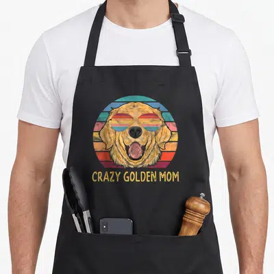 Golden cooking with dog apron - Retro golden retriever face with striped sunglasses and CRAZY GOLDEN MOM text below — shown on a black cotton canvas apron against a white background