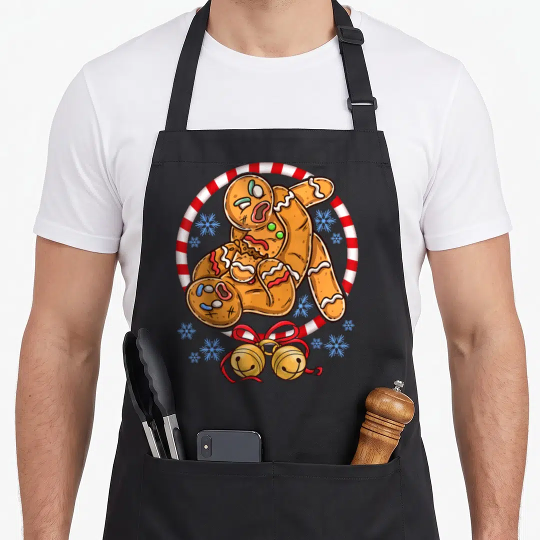 Fighting women's christmas aprons - Two gingerbread men wrestling inside a candy cane ring with gold bells and blue — shown on a black cotton canvas apron against a white background