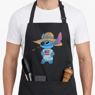 Americana novelty apron - Blue cartoon character wearing tan hat and holding wheat stalk on black apron — shown on a black cotton canvas apron against a white background