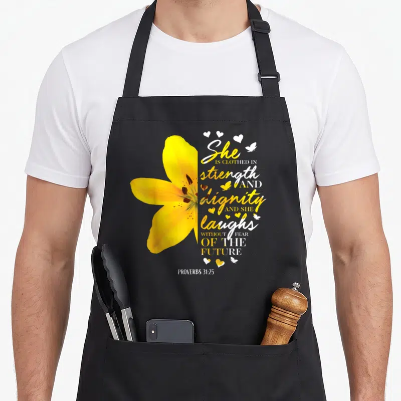 Flower bible verse apron - Yellow lily next to Proverbs 31:25 text with hearts and butterflies — shown on a black cotton canvas apron against a white background