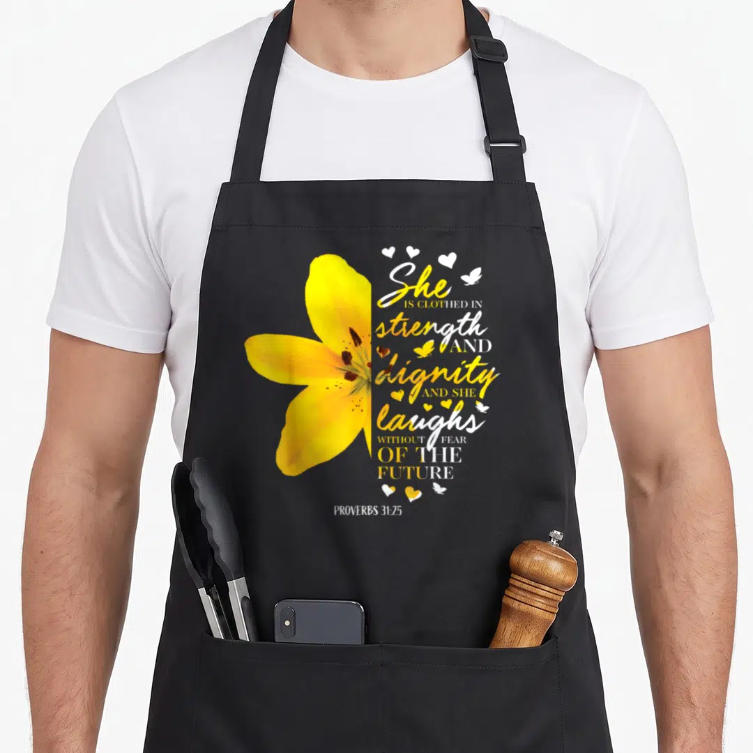 Flower bible verse apron - Yellow lily next to Proverbs 31:25 text with hearts and butterflies — shown on a black cotton canvas apron against a white background