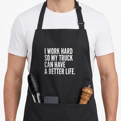 Owner truck apron - White stacked text reading I WORK HARD SO MY TRUCK CAN HAVE A BETTER LIFE — shown on a black cotton canvas apron against a white background
