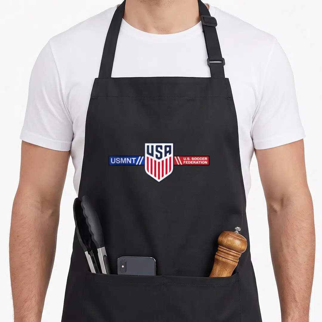 Soccer american football apron - Central USA shield with red stripes, blue USMNT banner, and red U.S. Soccer Federation — shown on a black cotton canvas apron against a white background