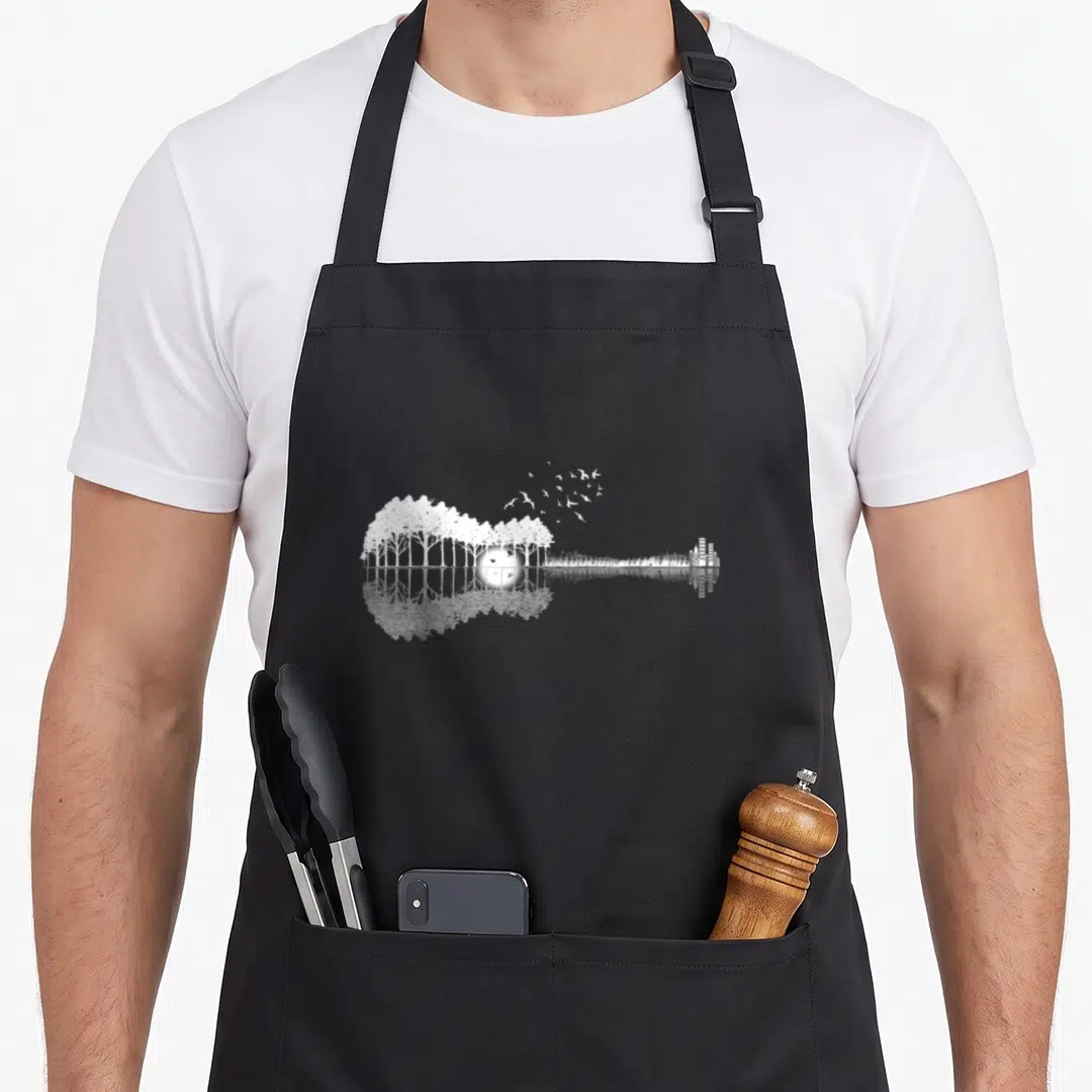 Guitar consistency apron - White silhouette of trees, sun, birds, and buildings forming a guitar shape with water — shown on a black cotton canvas apron against a white background