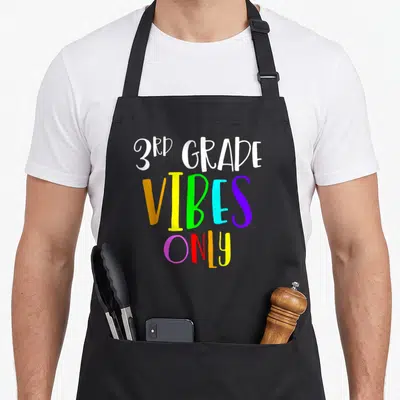 3rd grade student aprons - Stacked 3rd GRADE VIBES ONLY text in white, orange, yellow, green, cyan, purple, pink — shown on a black cotton canvas apron against a white background