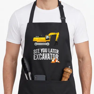 See backhoe girl apron - Cartoon yellow excavator with See You Later Excavator text and two orange traffic cones — shown on a black cotton canvas apron against a white background