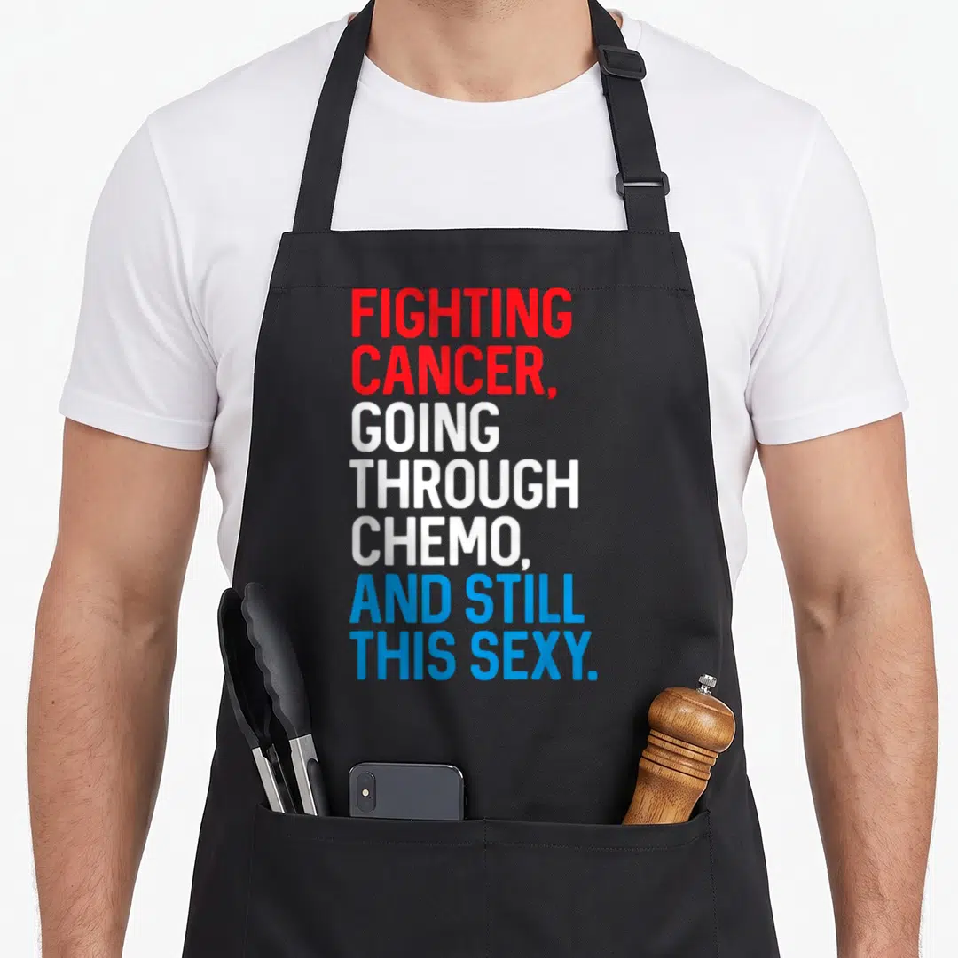 Fighting cancer man apron - Red white and blue stacked typography reading Fighting Cancer Going Through Chemo And Still — shown on a black cotton canvas apron against a white background