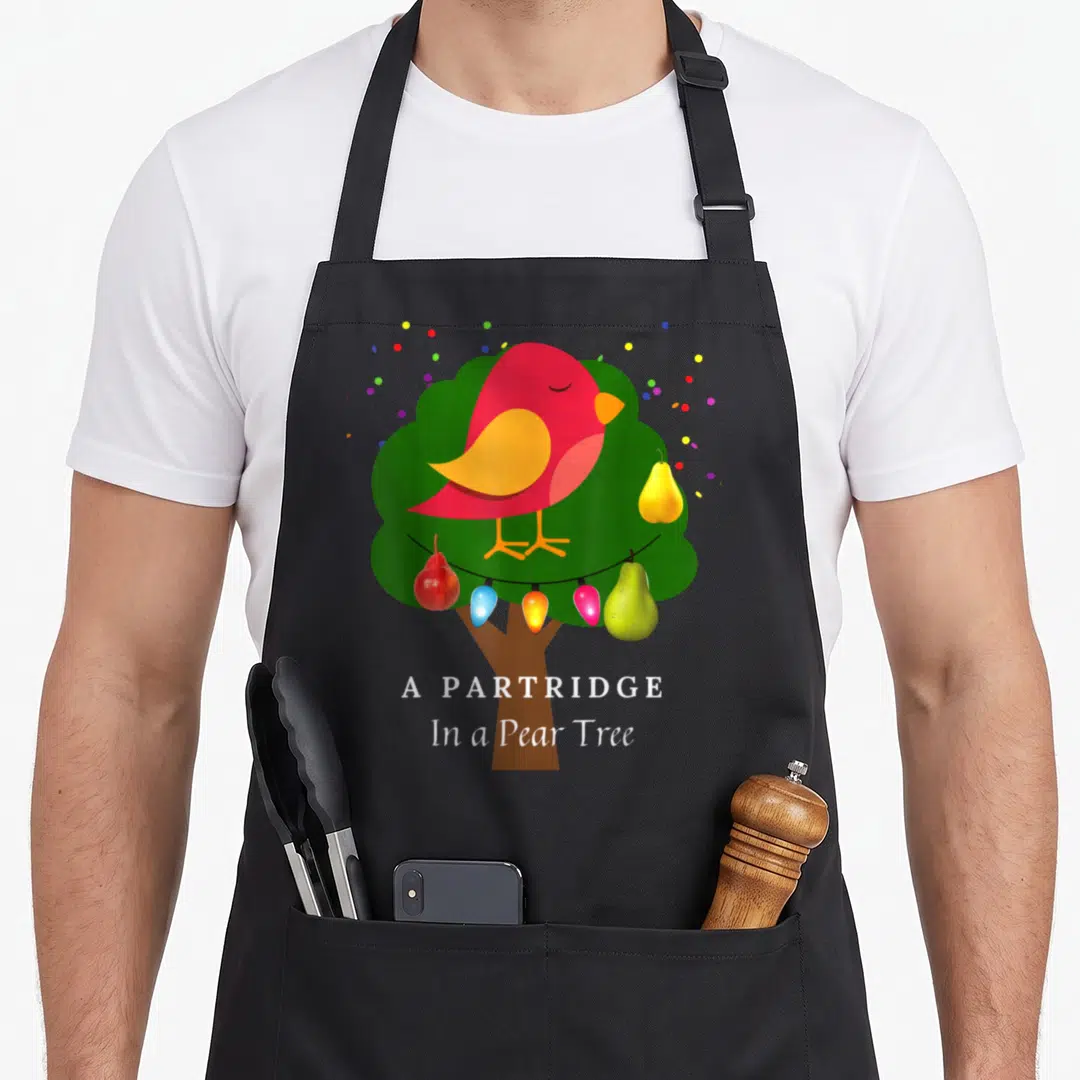 Twelve christmas tree apron - Red bird atop green tree with pears and lights below stacked white text — shown on a black cotton canvas apron against a white background