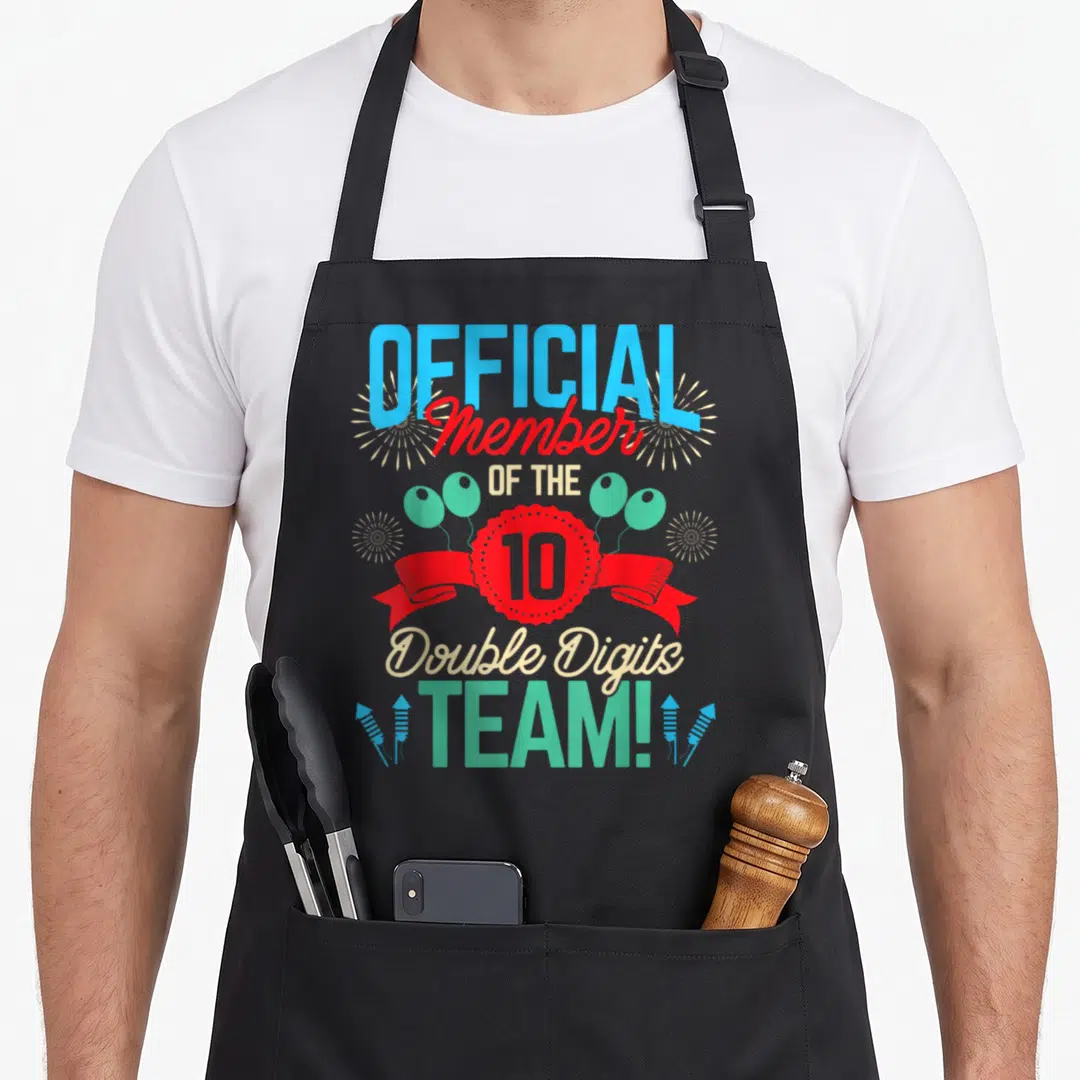 Digit twin birthday apron - Official Member of the 10 Double Digits Team text with red ribbon, balloons, and fireworks — shown on a black cotton canvas apron against a white background