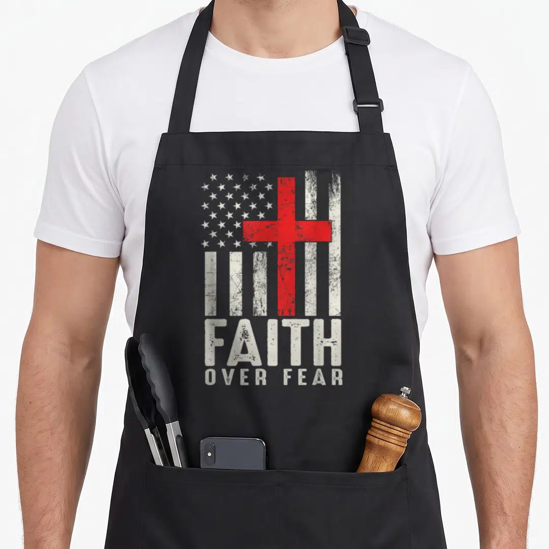 Faith fear american flag apron - Red cross over distressed grey and white stars and stripes with stacked FAITH — shown on a black cotton canvas apron against a white background