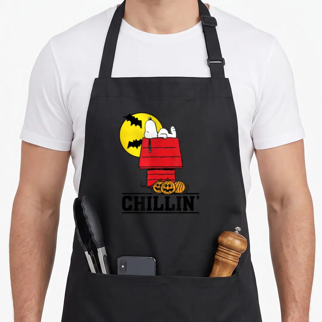 Chillin halloween apron - Snoopy on red doghouse with three pumpkins and yellow moon — shown on a black cotton canvas apron against a white background