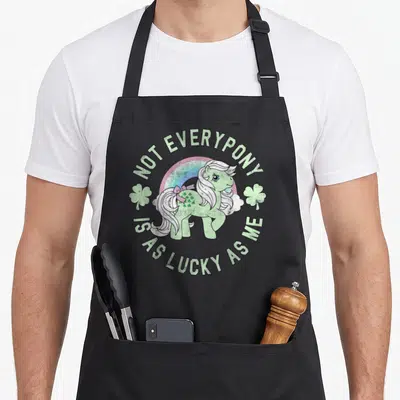 Minty st patrick day aprons - Cartoon pony with rainbow and shamrocks surrounded by text NOT EVERYPONY IS AS LUCKY AS ME — shown on a black cotton canvas apron against a white background
