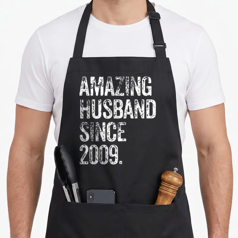 Amazing wedding aprons - White stacked text reading amazing husband since 2009 on a black background — shown on a black cotton canvas apron against a white background