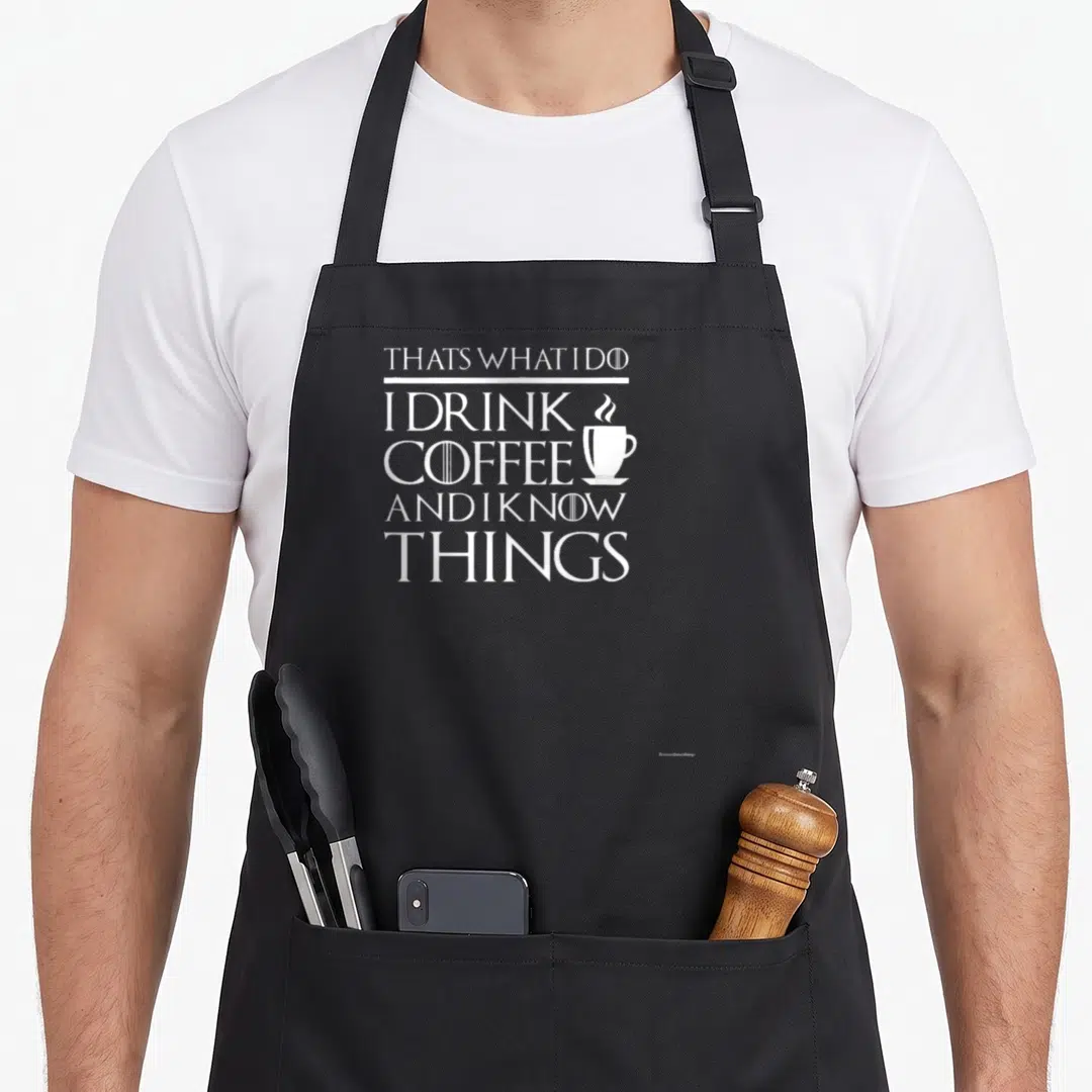 Funny drink coffee apron - White stacked text THATS WHAT I DO I DRINK COFFEE AND I KNOW THINGS with small steaming cup — shown on a black cotton canvas apron against a white background