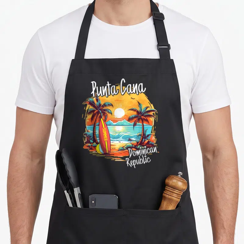 Dominican family aprons - Punta Cana beach scene with palm trees, summer surfboard, and Dominican Republic text — shown on a black cotton canvas apron against a white background