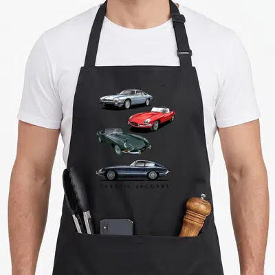 Cute sport car apron - Four classic Jaguars in silver, red, green, blue, black with CLASSIC JAGUARS text — shown on a black cotton canvas apron against a white background