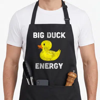 Rubber meme apron - Yellow rubber duck with orange beak between white Big Duck Energy text — shown on a black cotton canvas apron against a white background