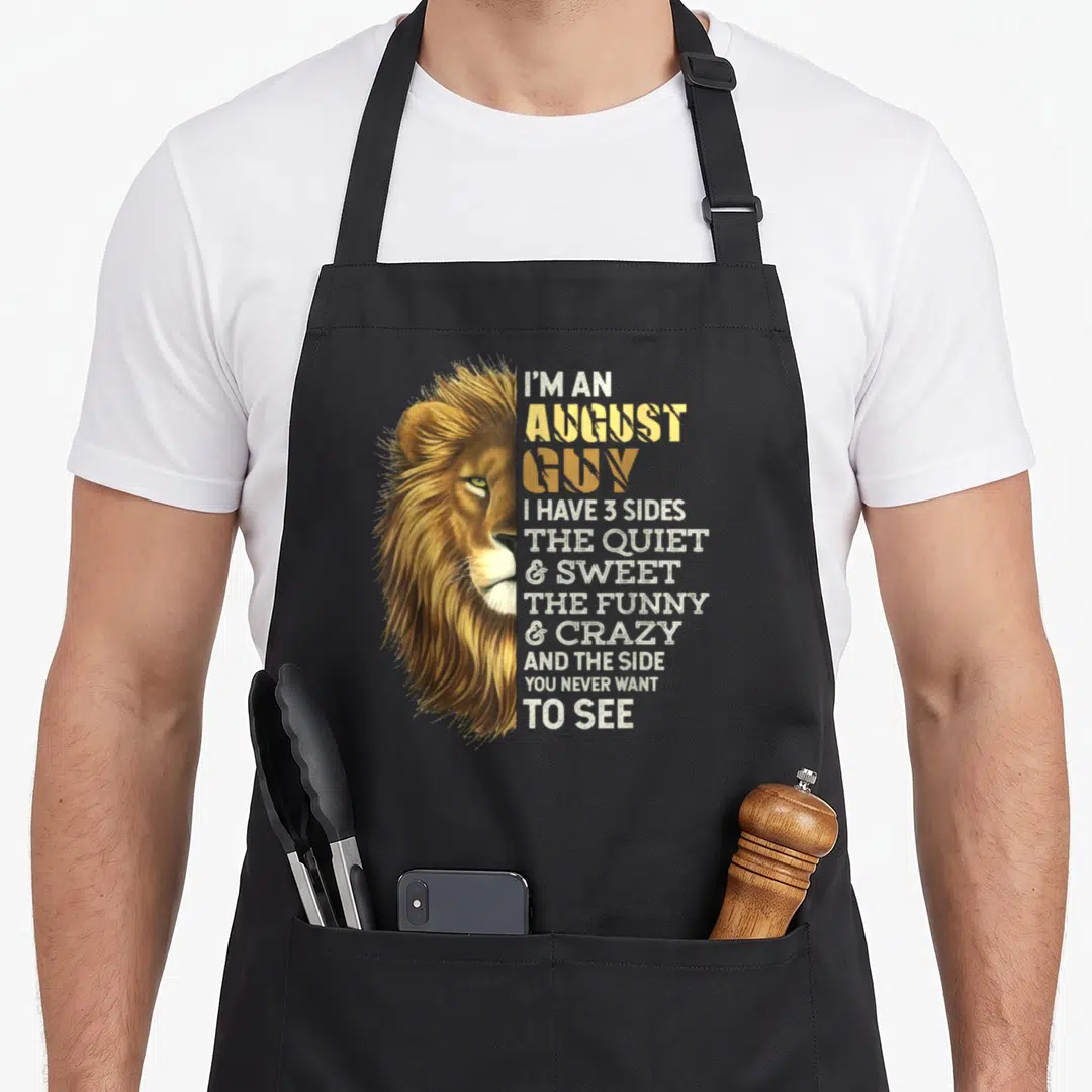 Lion birthday apron - Realistic lion head beside stacked text listing three personality sides in gold and white — shown on a black cotton canvas apron against a white background