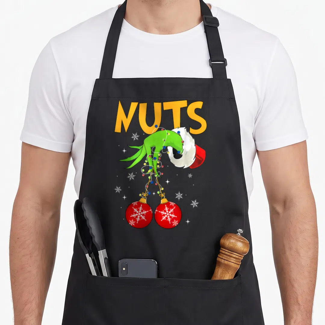 Snow couples christmas aprons - NUTS text above green hand holding two red ornaments with lights and snowflakes — shown on a black cotton canvas apron against a white background