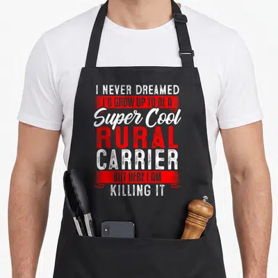 Rural carrier postal aprons - White and red stacked text reading I Never Dreamed I'd Grow Up To Be A Super Cool Rural — shown on a black cotton canvas apron against a white background