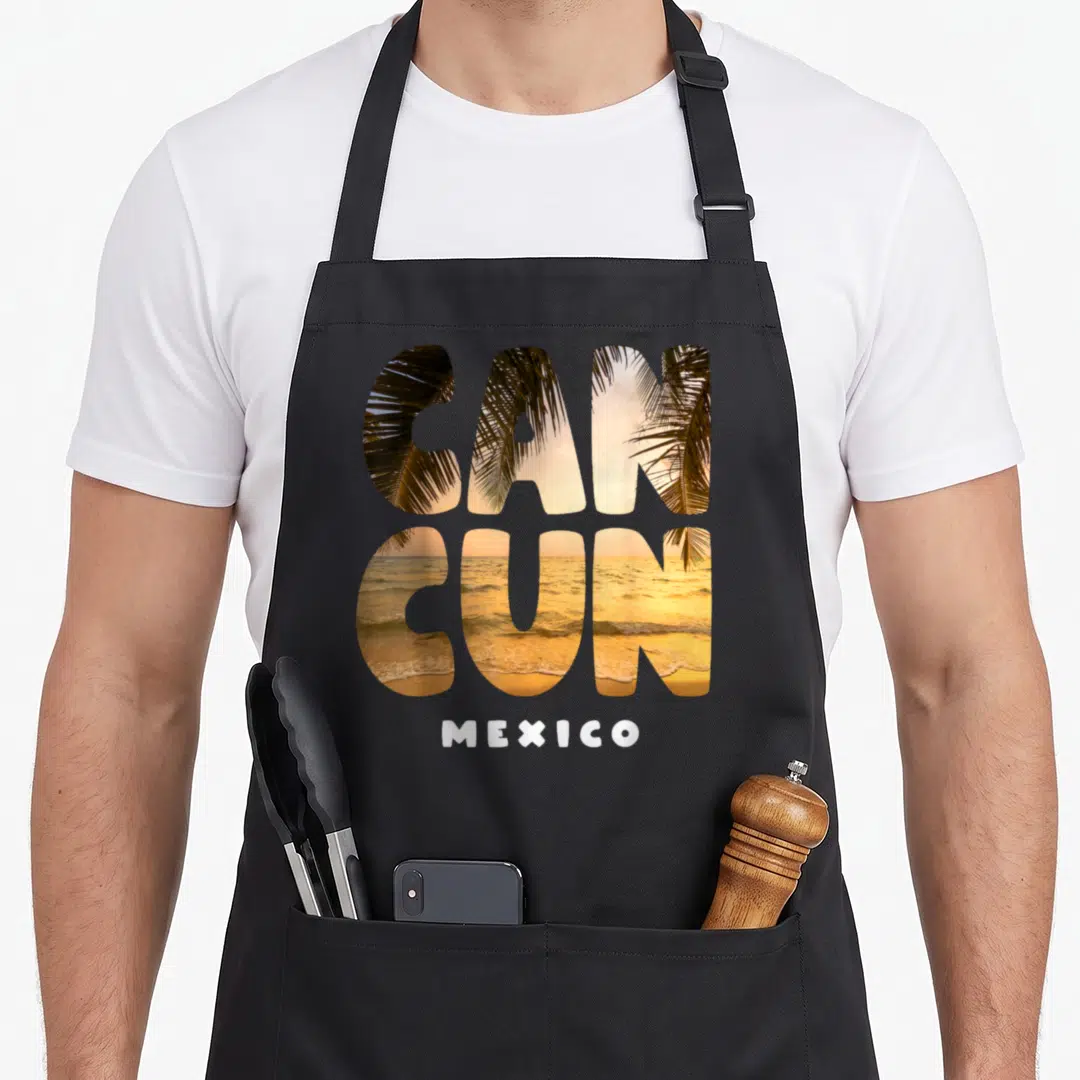 Sunset summer mexico apron - CANCUN letters filled with beach scene and MEXICO text below — shown on a black cotton canvas apron against a white background