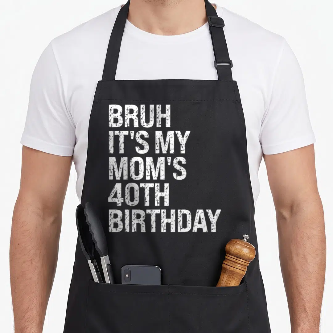 Bruh queen of baking apron - White stacked text reading BRUH IT'S MY MOM'S 40TH BIRTHDAY on black background — shown on a black cotton canvas apron against a white background