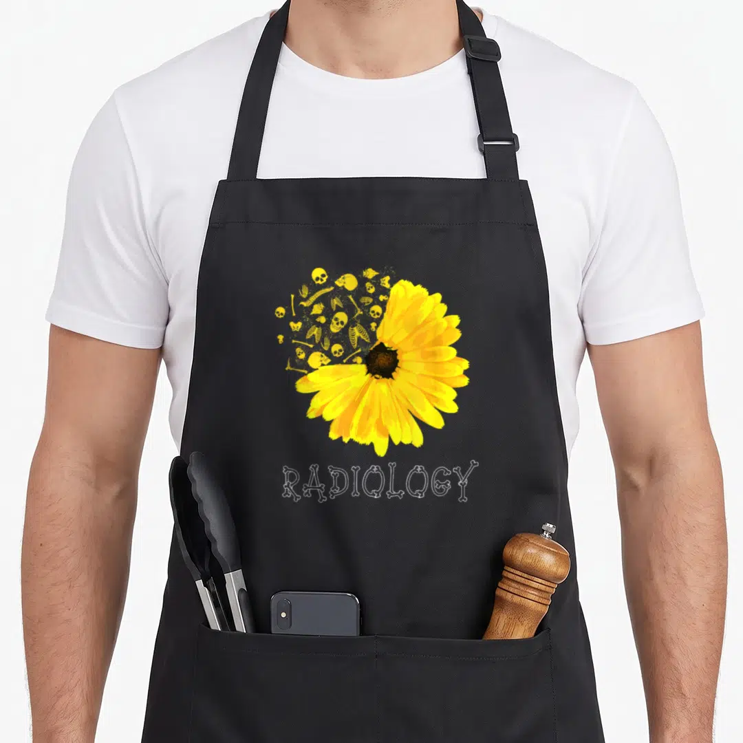 Sunflower x ray apron - Yellow flower dissolving into yellow skulls and bones with white bone-font RADIOLOGY text below — shown on a black cotton canvas apron against a white background