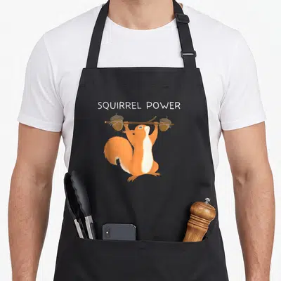 Power squirrel aprons - Cartoon squirrel lifting branch with two acorns under SQUIRREL POWER text — shown on a black cotton canvas apron against a white background