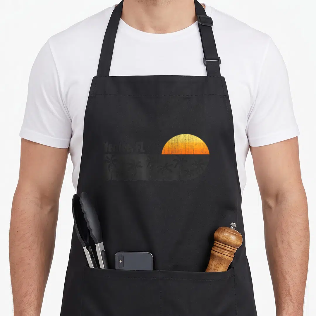 Venice pride apron - Retro Venice FL text above grey palm tree rectangle and yellow orange semi-circle sunset — shown on a black cotton canvas apron against a white background