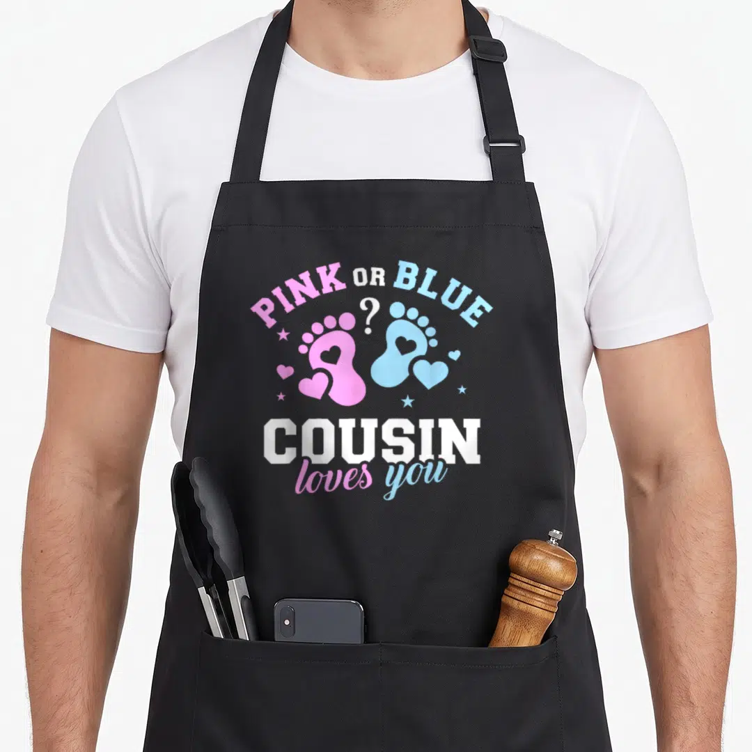 Cousin gender reveal co apron - Pink and blue baby footprints with hearts stars and text cousin loves you — shown on a black cotton canvas apron against a white background