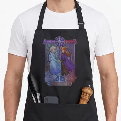 Frozen split apron - Elsa and Anna in purple frame with FROZEN text at bottom — shown on a black cotton canvas apron against a white background