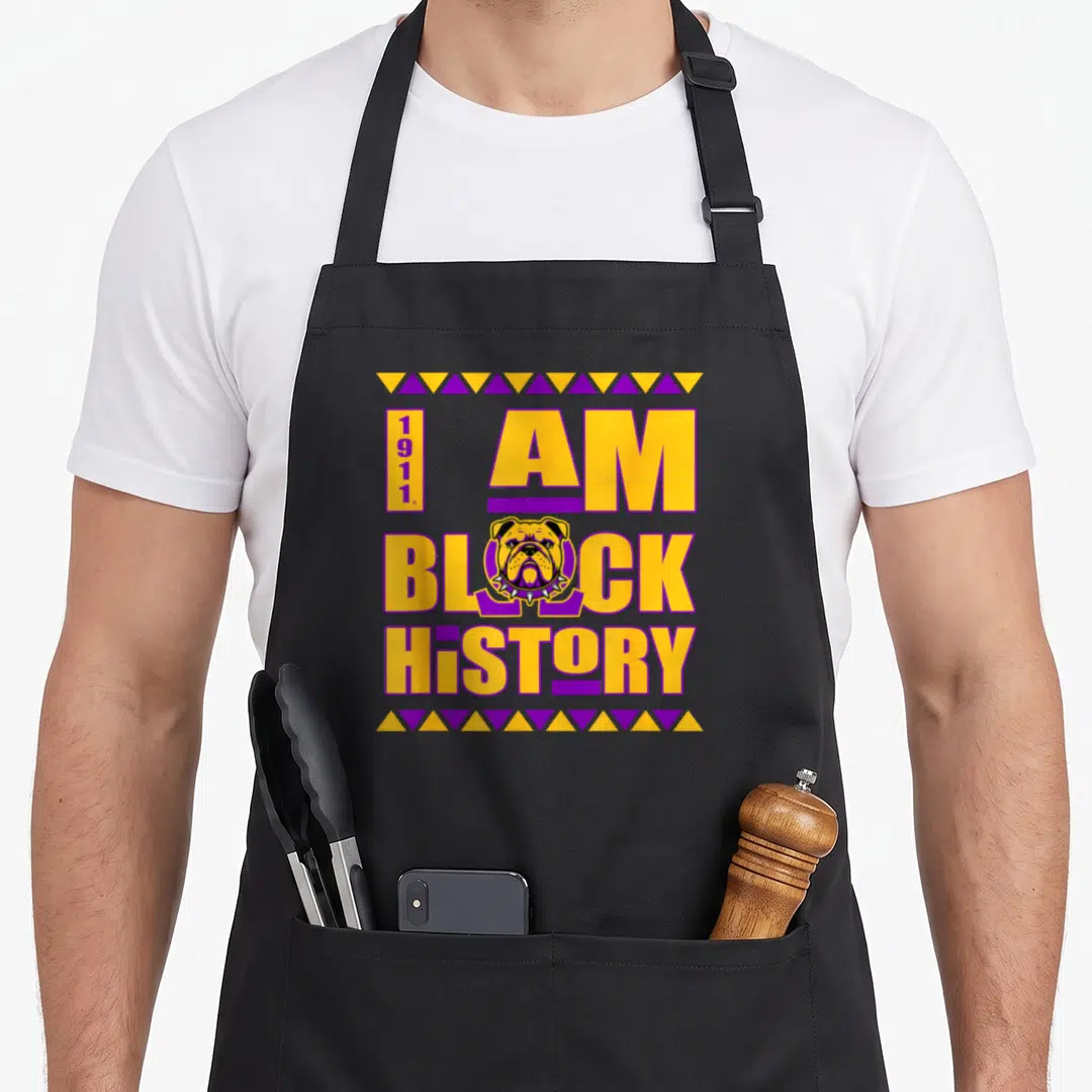 Paraphernalia fraternity apron - I AM BLOCK HISTORY text with bulldog head and 1911 in yellow purple triangles — shown on a black cotton canvas apron against a white background
