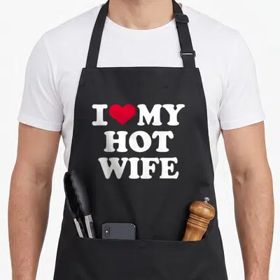 Cute hot wife apron - White text reading I MY HOT WIFE with a red heart between I and MY — shown on a black cotton canvas apron against a white background