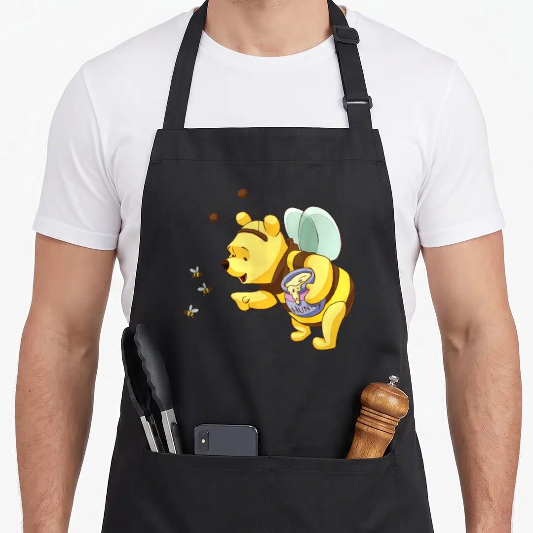 Costume honey bee apron - Winnie the Pooh in bee costume holding HUNNY pot with three bees — shown on a black cotton canvas apron against a white background