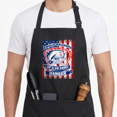 Grandpa rangers apron - Distressed US flag background with shield, beret, crossed knives, and proud grandpa text — shown on a black cotton canvas apron against a white background