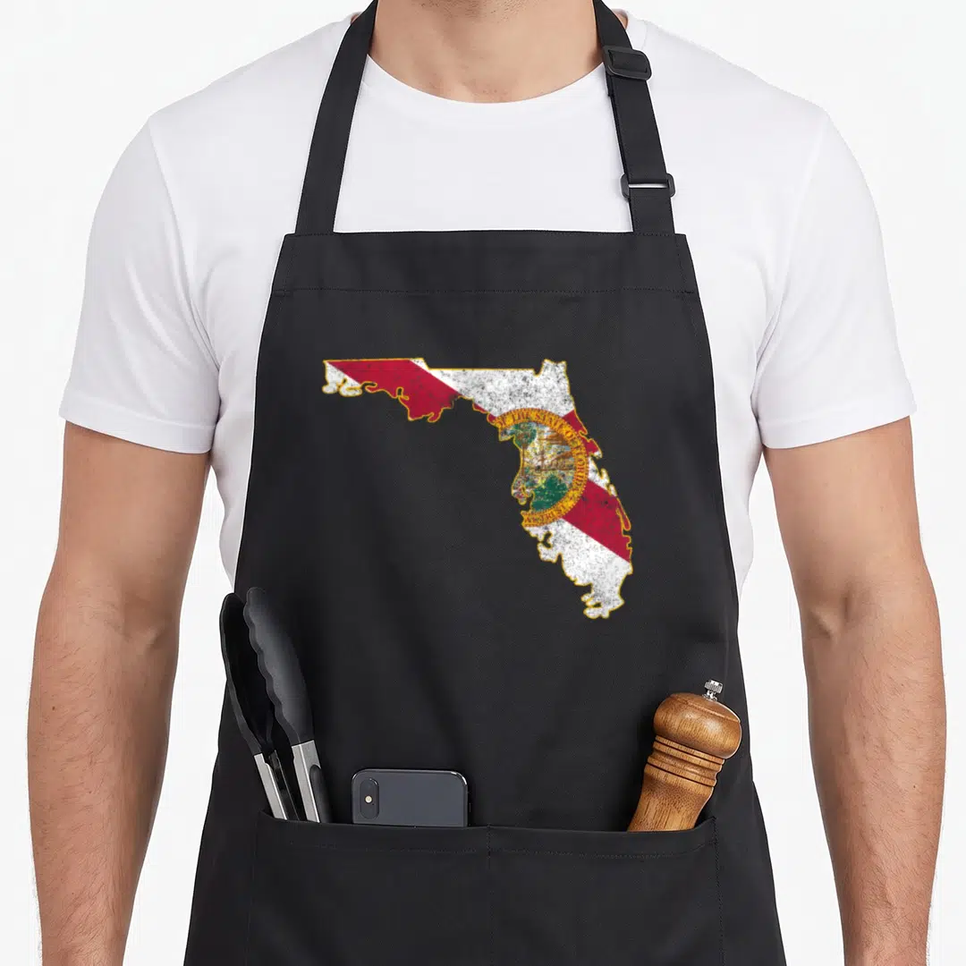 Shape florida apron - Distressed Florida state map in red white yellow and green with gold seal text — shown on a black cotton canvas apron against a white background
