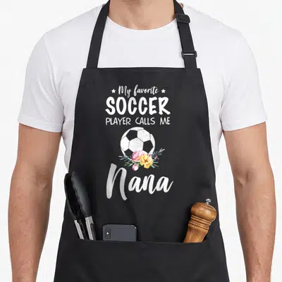 Soccer nana aprons - Soccer ball with pink yellow flowers and Nana text on black apron — shown on a black cotton canvas apron against a white background
